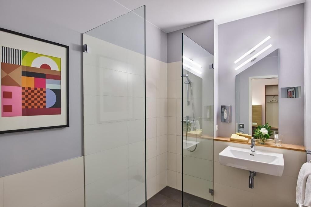 A modern bathroom with a glass shower enclosure, a white sink, and a mirror.
