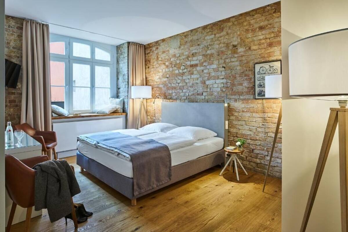 Un dormitorio con pared de ladrillo, una cama, un escritorio con silla y una ventana con cortinas.