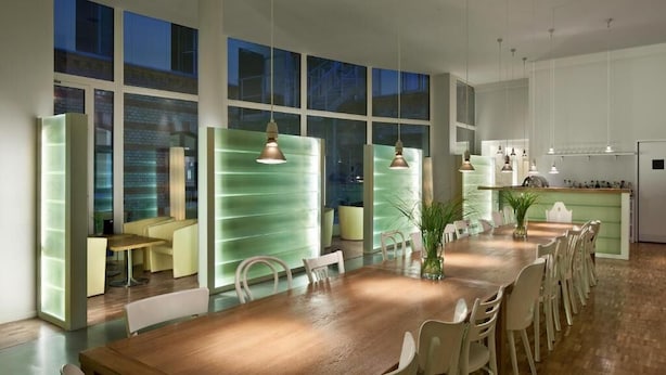A modern dining area with a long wooden table, chairs, and pendant lighting. - Hotel 38  (Berlin)