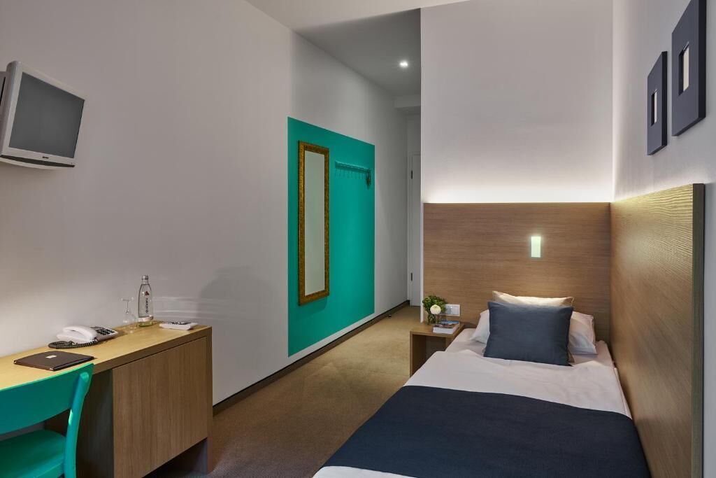 Une chambre d’hôtel avec un lit, un bureau, une chaise, une télévision et une porte.