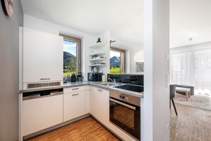 Eine moderne Küche mit weißen Schränken, einem eingebauten Backofen, einer Kaffeemaschine und Blick auf eine grüne Landschaft.