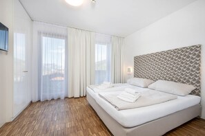 A hotel room with a large bed, white curtains, a patterned headboard, and a wooden floor. - Premium apartment #6.2  with 1 bedroom and sauna area (Rohrmoos-Untertal)