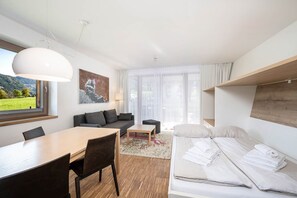 Ein modernes Hotelzimmer mit Essbereich, einer Couch, einem Bett und einem großen Fenster mit Blick ins Freie.