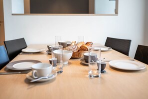 Ein Esstisch gedeckt mit Tellern, Schüsseln, Tassen und einem Brotkorb.