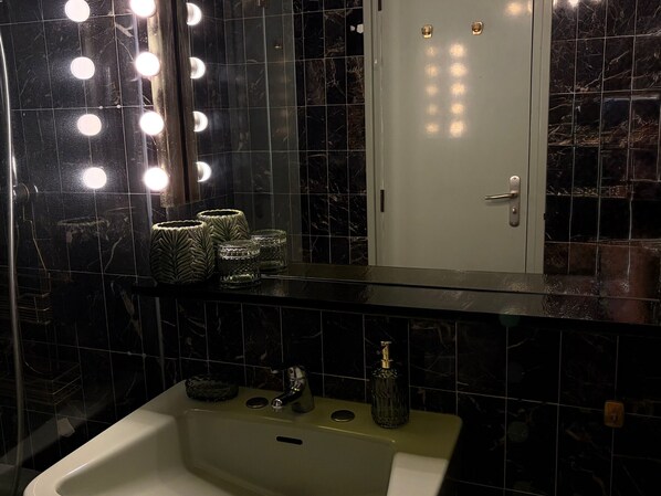 Um banheiro com toucador, pia, espelho com iluminação e porta.
