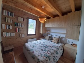 Ein Zimmer mit Holzboden, einem Bett, Bücherregalen und einem Fenster.