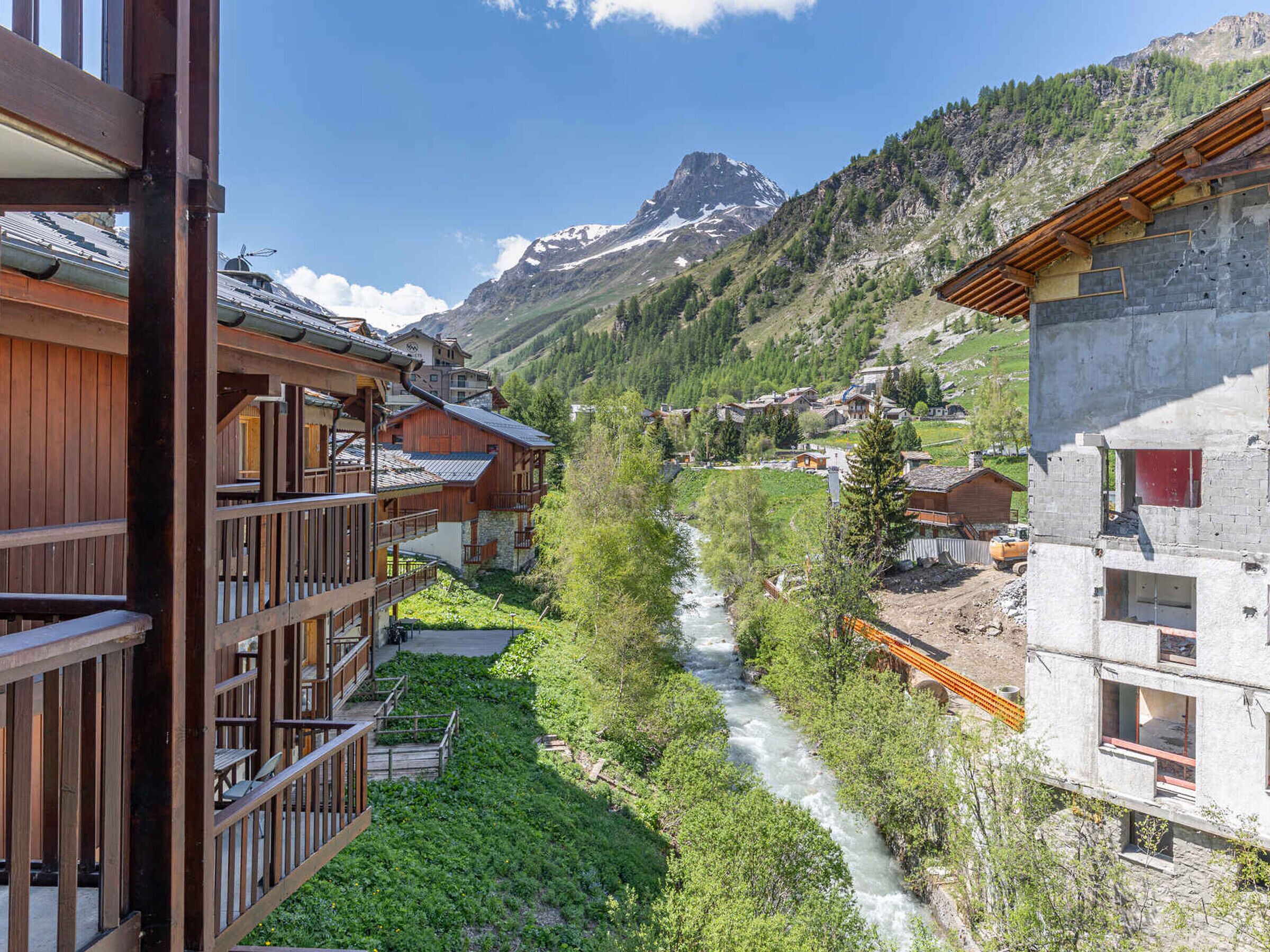 A mountain village with wooden buildings, a river, and a mountain in the background.