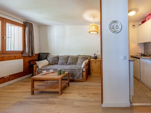 Ein gemütliches Wohnzimmer mit einer Couch, einem Holztisch, einer kleinen Kommode und einer Küchenzeile mit Herd und Schränken.