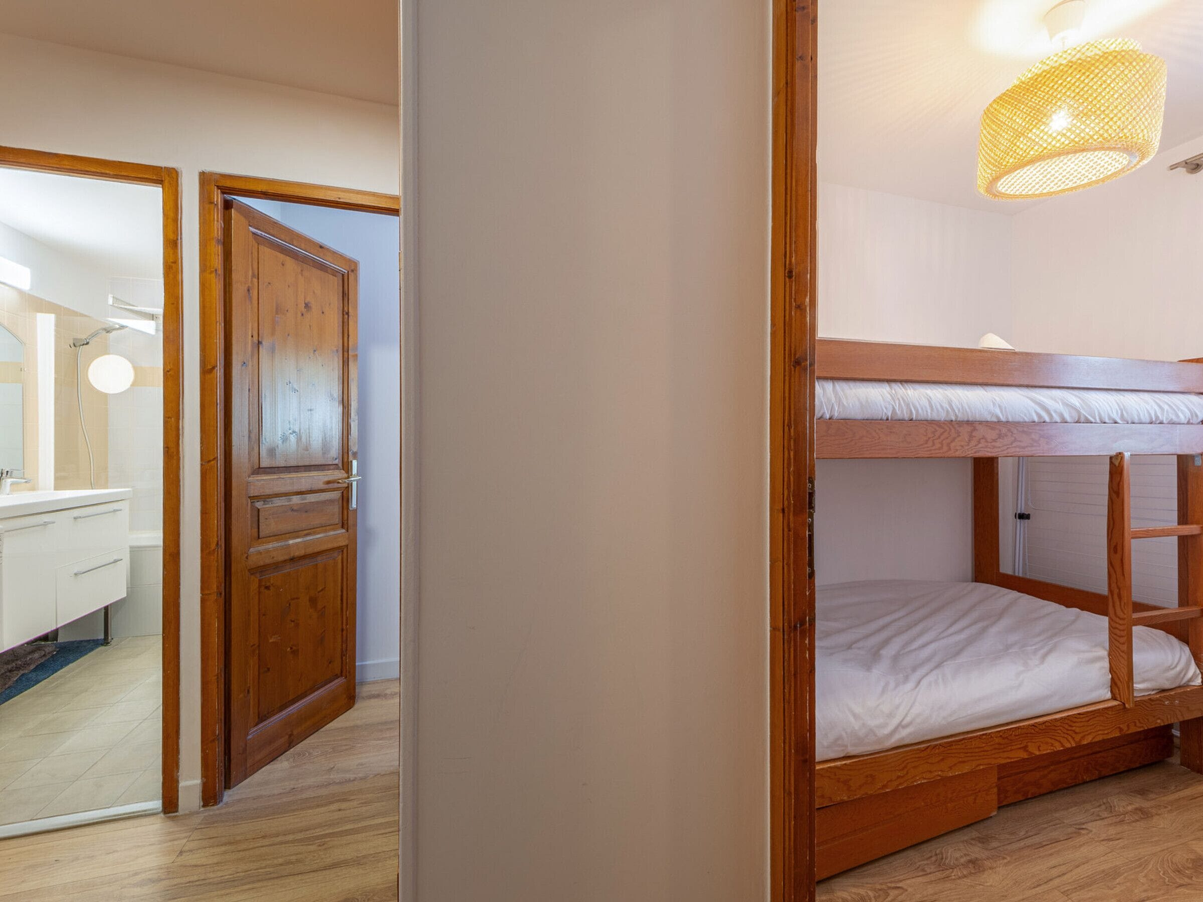A bunk bed with a wooden frame, a bathroom with a mirror and sink, and a door leading to another room.