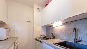 Moderni keittiö, jossa on valkoiset kaapit, harmaa työtaso, sisäänrakennettu astianpesukone ja musta pesuallas.