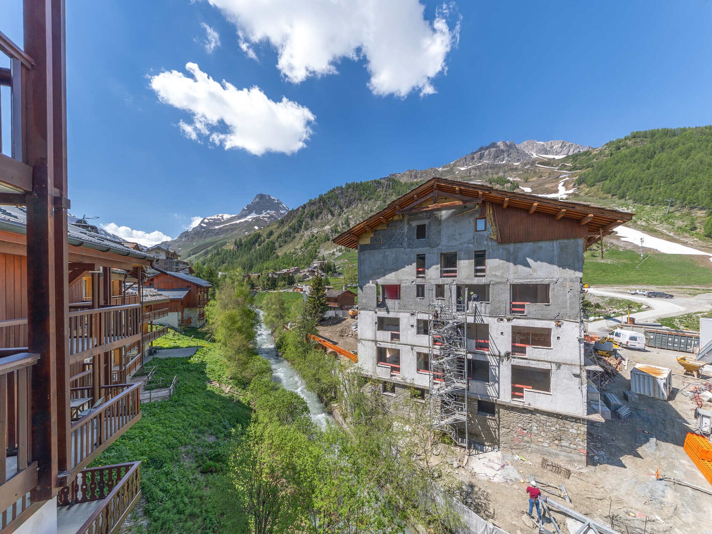 Eine Berglodge mit Holzausbau, ein Fluss, der durch das Anwesen fließt, und eine Ansicht eines schneebedeckten Berges im Hintergrund.