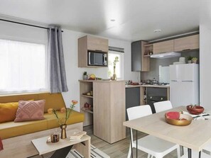 A compact living space with a sofa, a dining table, a kitchen area, and a microwave. - Cozy mobile home, air conditioning - 6 guests (Grayan-et-l'Hôpital)