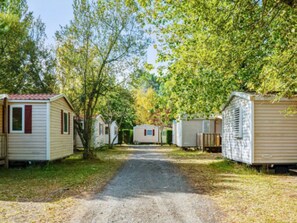 Une rangée de maisons mobiles, séparées par un chemin de gravier et entourées d’arbres.