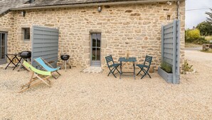 A stone building with a gravel driveway, a table with chairs, and a hammock. - Charming cottage in Clis - 2 guests (Guérande)