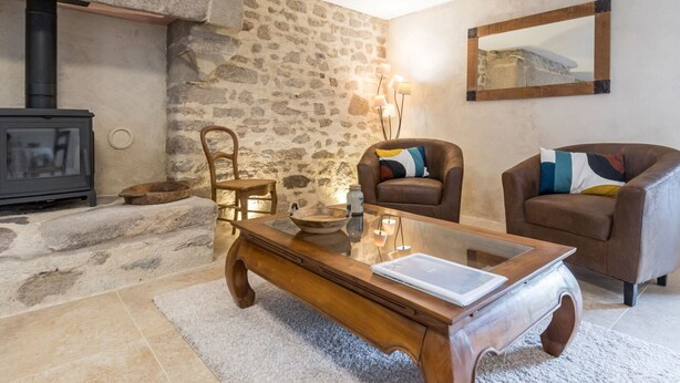 A stone-walled living room with a fireplace, a wooden coffee table, two leather armchairs, and a mirror on the wall. - Charming cottage in Clis - 2 guests (Guérande)