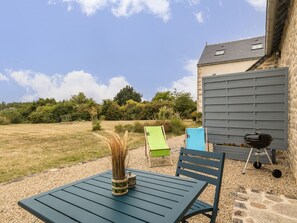 Eine Terrasse im Freien mit Tisch, Stühlen, Grill und einer Steinmauer.