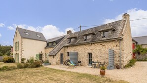 A stone building with a sloped roof, a small garden area with a swing set, and a gravel driveway. - Charming cottage in Clis - 2 guests (Guérande)