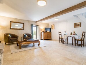 A spacious living area with a wooden coffee table, two armchairs, a television, and a dining table with chairs. - Charming cottage in Clis - 2 guests (Guérande)