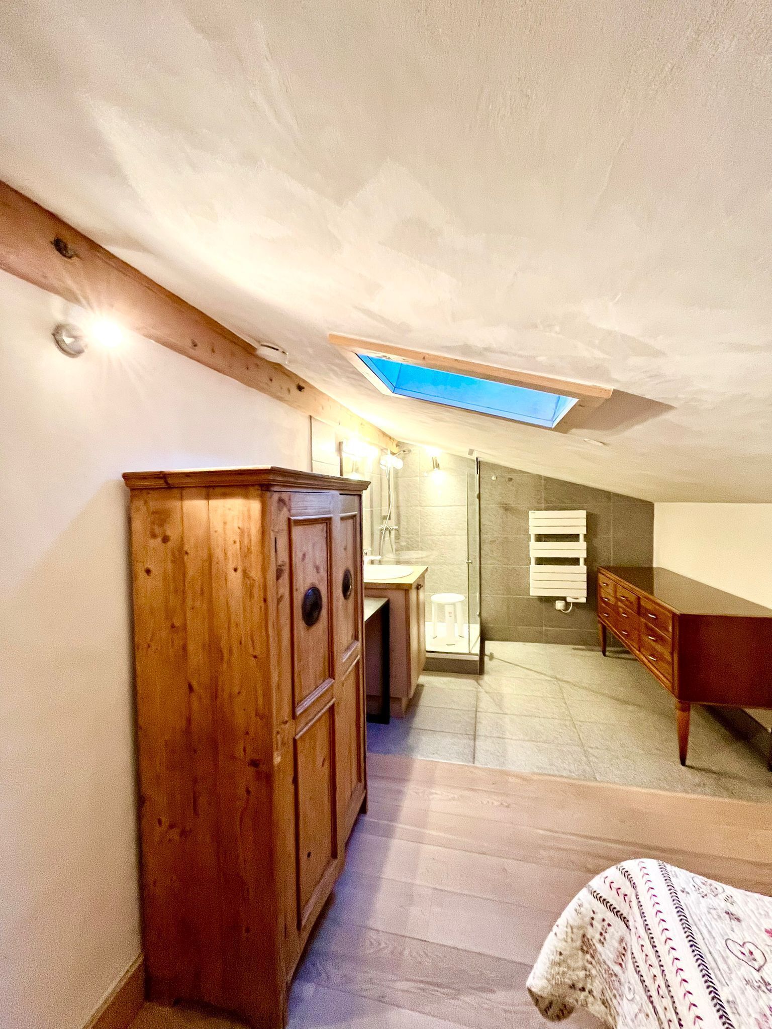 Une chambre avec un puits de lumière, une armoire en bois, une table de chevet et un lit.