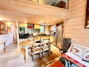 Une cuisine moderne équipée d’appareils électroménagers en acier inoxydable, un coin repas avec des meubles en bois et un espace de vie chaleureux agrémenté d’un canapé et de coussins décoratifs.