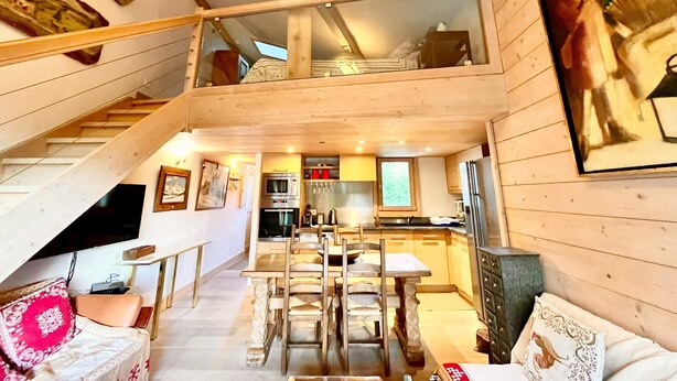 A multi-level wooden cabin with a dining area, kitchen, and a staircase. - Charming apartment facing Mont Blanc (combloux)