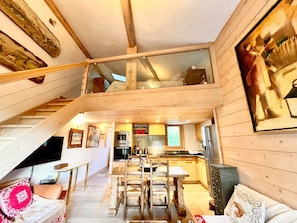 A multi-level wooden cabin with a dining area, kitchen, and a staircase. - Charming apartment facing Mont Blanc (combloux)