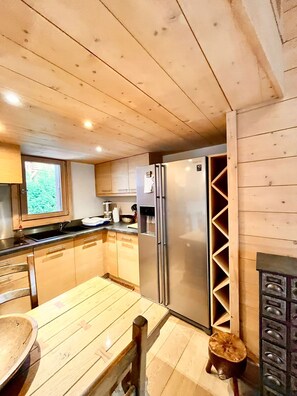 Une cuisine aux murs lambrés, équipée d’un réfrigérateur, d’un évier et d’une table en bois.
