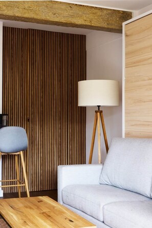 Ein Zimmer mit einer Wand aus Holzlatten, einem grauen Sofa, einem Holztisch, einem blauen Sessel und einer Stehlampe.