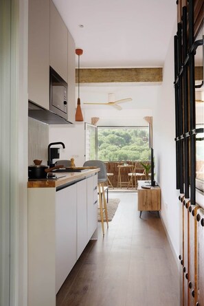 A modern kitchen with a dining area, large windows, and a view of greenery. - La Escondida Rural (San Martín de Valdeiglesias)