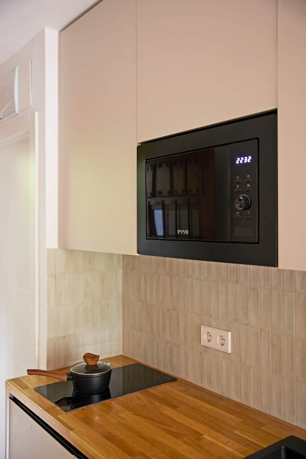 Una cocina con microondas integrado, encimera de madera y salpicadero de azulejos.