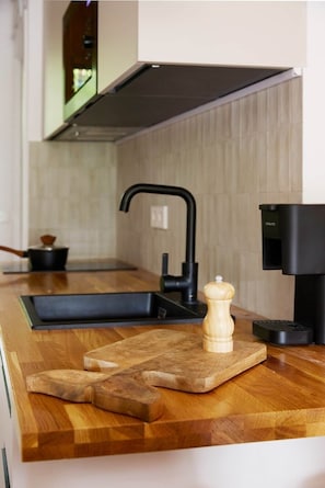 A modern kitchen with a wooden countertop, a black faucet, a cutting board, and a pepper grinder. - La Escondida Rural (San Martín de Valdeiglesias)