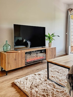 A modern living room with a flat-screen TV on a wooden TV stand, a fluffy rug, and a potted plant. - La Escondida Apartment at the San Juan B Reservoir (San Martín de Valdeiglesias)