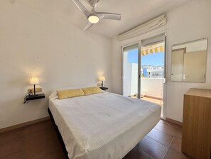 Ein Schlafzimmer mit einem Bett, zwei Nachttischlampen, einem Deckenventilator, einer Schiebeglastür zum Balkon und einem Holzschrank.
