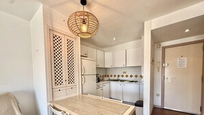 Een keuken met witte kasten, een eettafel met stoelen, een hanglamp en een betegelde spatwand.