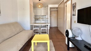 Een woonkamer met een bank, een gele tafel, een televisie en een ventilator.