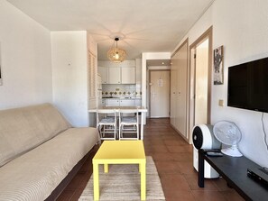 Ein Wohnzimmer mit einer Couch, einem gelben Tisch, einem Fernseher und einem Ventilator.
