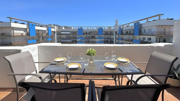 Een terras op het dak met een tafel gedekt voor twee personen, met uitzicht op een woongebied met blauwe gebouwen.