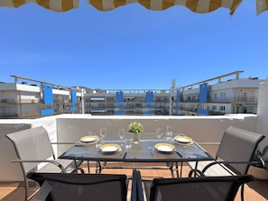 Eine Dachterrasse mit gedecktem Tisch für zwei Personen, mit Blick auf ein Wohngebiet mit blauen Gebäuden.