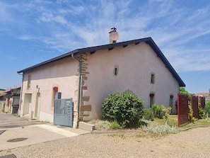 A two-story building with a stone facade, a blue door, and a small garden area.
