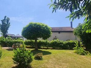 A well-maintained garden with a neatly trimmed tree, a lawn, and a building with a tiled roof.
