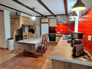 A dining area with a table, chairs, a fireplace, and a kitchen with red tiles.