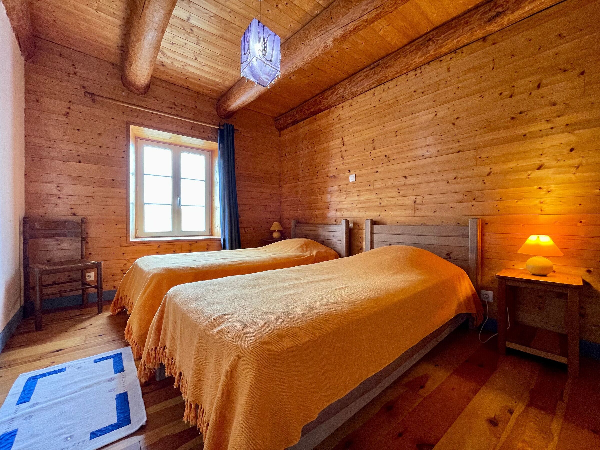 A wooden room with two beds, a window, a chair, and a lamp.