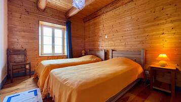 A wooden room with two beds, a window, a chair, and a lamp.