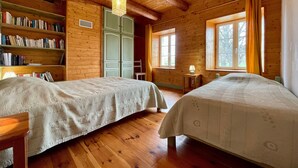A wooden cabin with two beds, a bookshelf, and a window with curtains.