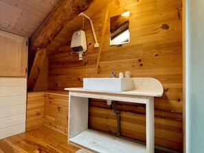 L’intérieur d’une cabane en bois, avec un évier blanc, un miroir et un radiateur fixé au plafond.
