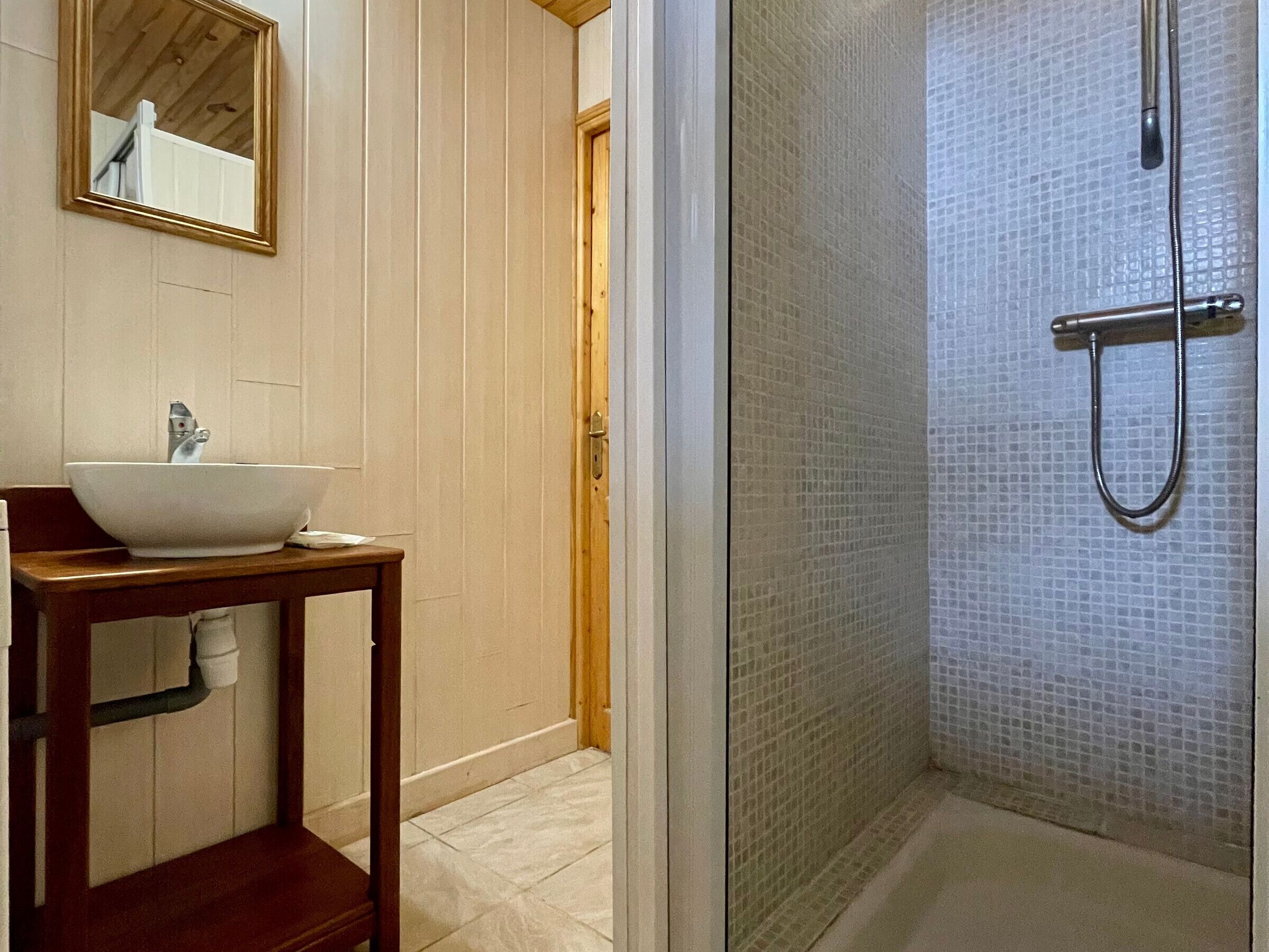 Une salle de bain avec un lavabo blanc, un meuble-lavabo en bois et une cabine de douche en verre.