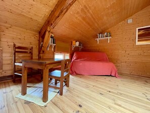 Eine Holzhütte mit Esstisch, Stühlen, einer roten Couch und Bücherregalen.