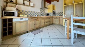 A kitchen with wooden cabinets, a microwave, a sink, and a dining area with a table and chairs. - Rustic family retreat in the Allier Gorges, nature and hiking nearby (Alleyras)