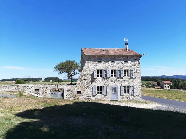 A stone building with a red-tiled roof, multiple windows, and a chimney.