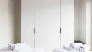 Quarto de hotel com cama, duas toalhas enroladas e um guarda-roupa com espelho.